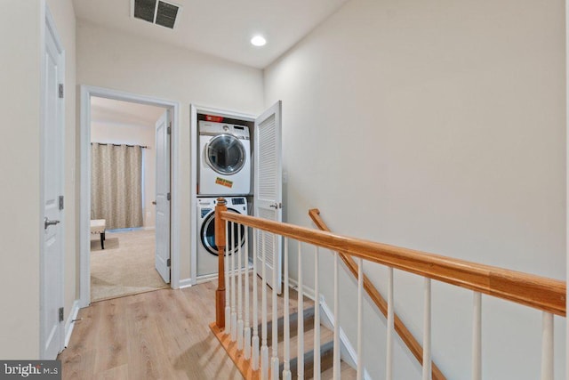 hall with estacked washer and dryer, an upstairs landing, and light wood-style flooring