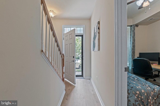 foyer entrance featuring light wood-type flooring, baseboards, stairway, and a ceiling fan