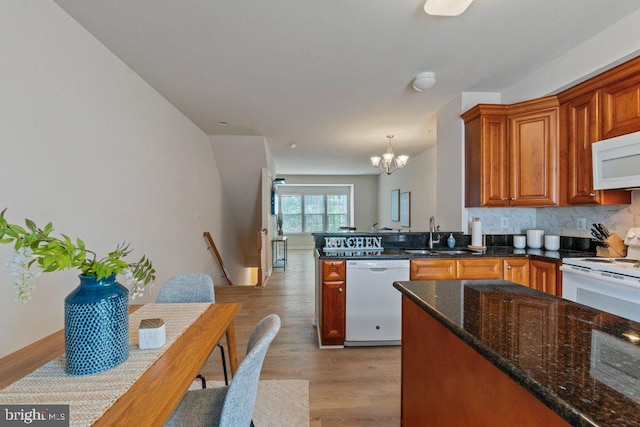 kitchen featuring white appliances, a sink, a chandelier, light wood finished floors, and decorative backsplash