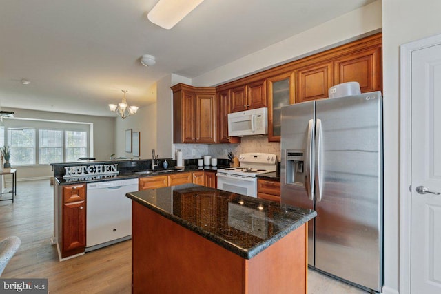 kitchen featuring white appliances, a sink, a chandelier, brown cabinetry, and a peninsula