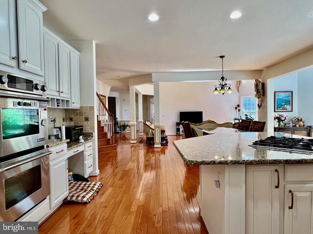 4718 Village Dr, Fairfax, VA 22030 - kitchen with stainless steel appliances, white cabinets, tasteful backsplash, light wood-style flooring, and dark stone counters