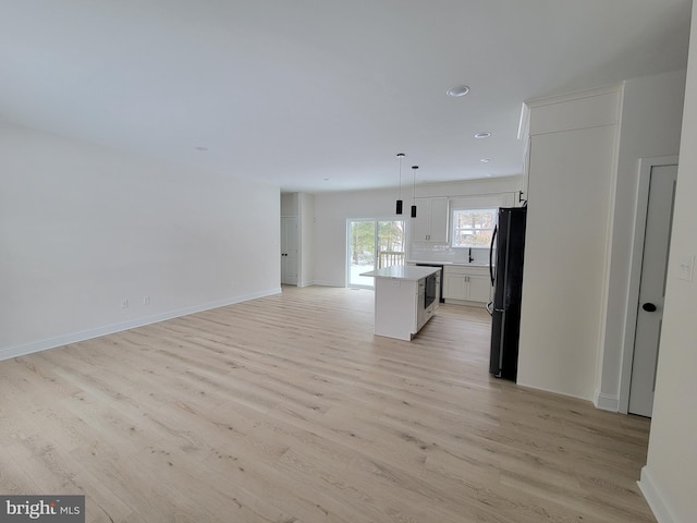 unfurnished living room with light wood-type flooring, recessed lighting, a sink, and baseboards