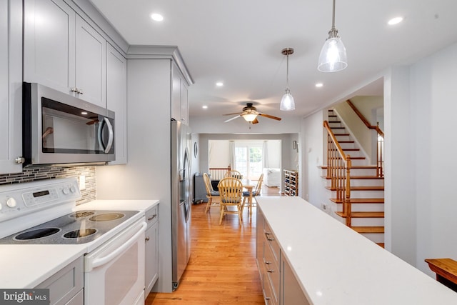 kitchen featuring appliances with stainless steel finishes, light wood-type flooring, light countertops, backsplash, and hanging light fixtures