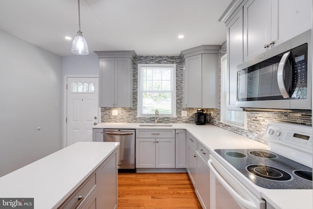 kitchen featuring appliances with stainless steel finishes, a sink, gray cabinetry, backsplash, and light countertops