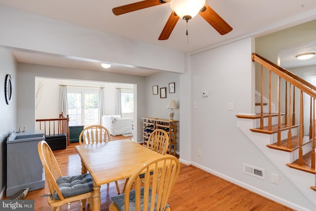 dining area featuring light wood-style floors, stairway, baseboards, and a ceiling fan