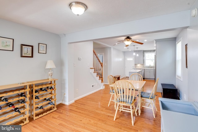 dining room featuring stairway, light wood-style floors, ceiling fan, and baseboards