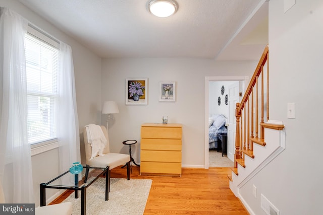 sitting room featuring healthy amount of natural light, stairs, light wood-style flooring, and baseboards
