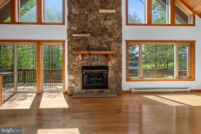 2107 Lenape Ter, Canadensis, PA 18325 - unfurnished living room featuring a baseboard heating unit, plenty of natural light, wood finished floors, high vaulted ceiling, and a stone fireplace