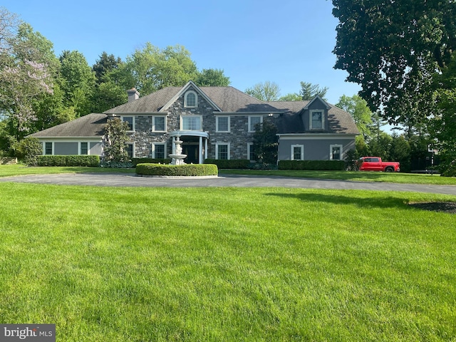 view of front of house featuring stone siding, a front lawn, and a chimney