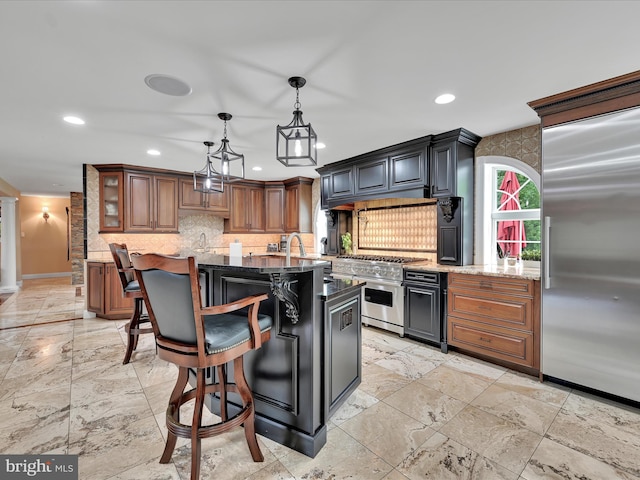 kitchen featuring high quality appliances, backsplash, recessed lighting, stone counters, and a center island with sink