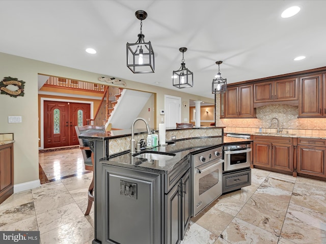 kitchen with a sink, stainless steel oven, backsplash, an island with sink, and recessed lighting
