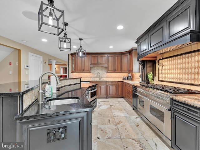 kitchen with a sink, range with two ovens, a center island with sink, dark stone countertops, and recessed lighting