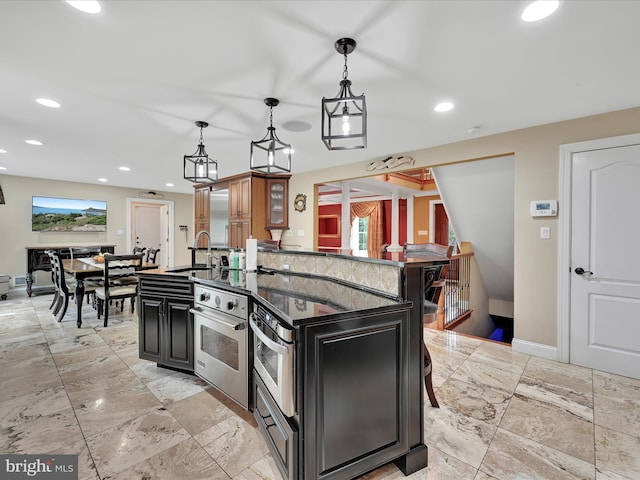 kitchen with a center island with sink, stainless steel oven, a sink, baseboards, and recessed lighting