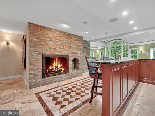 kitchen with dark stone counters, recessed lighting, a fireplace, stone tile floors, and a kitchen bar