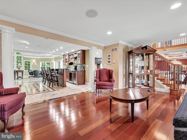 living area featuring ornate columns, light wood finished floors, stairs, ornamental molding, and recessed lighting