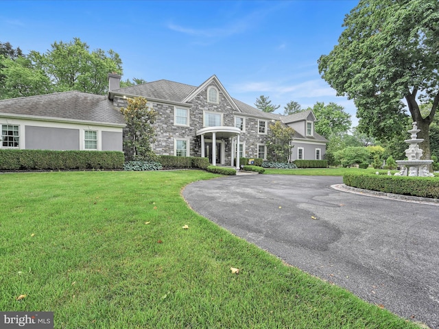 colonial inspired home featuring stone siding, a chimney, and a front yard