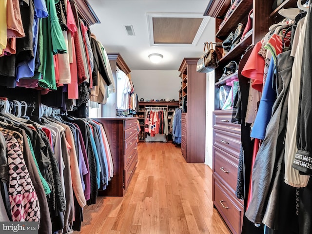 walk in closet with attic access and light wood-style floors