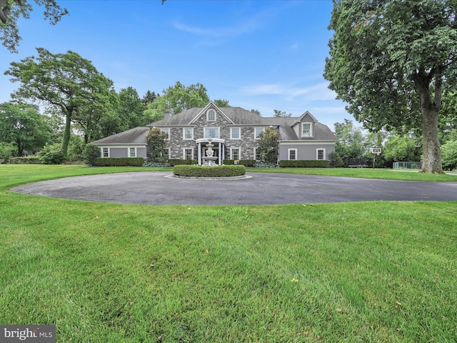 view of front facade with stone siding, a front lawn, and curved driveway