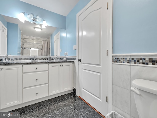 full bathroom featuring tile walls, wainscoting, a shower with curtain, toilet, and double vanity