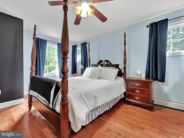 bedroom featuring multiple windows, light wood-type flooring, a baseboard heating unit, and ceiling fan