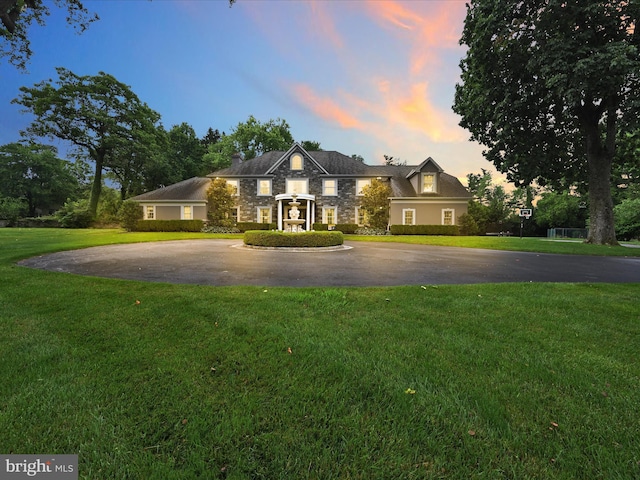 view of front of home featuring stone siding, curved driveway, a yard, and a chimney
