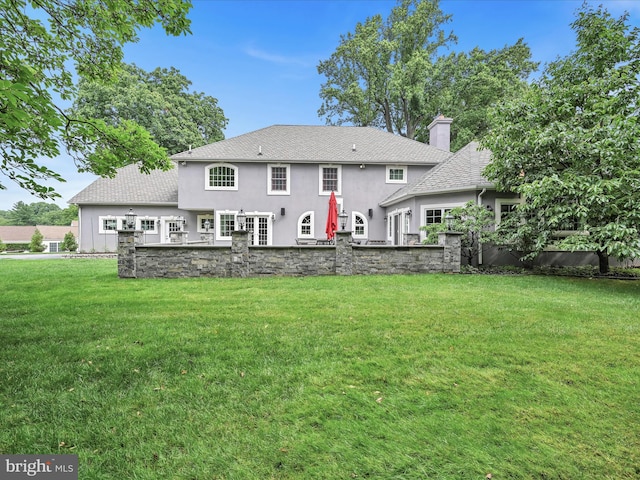 rear view of property with stucco siding, a chimney, a lawn, and a shingled roof