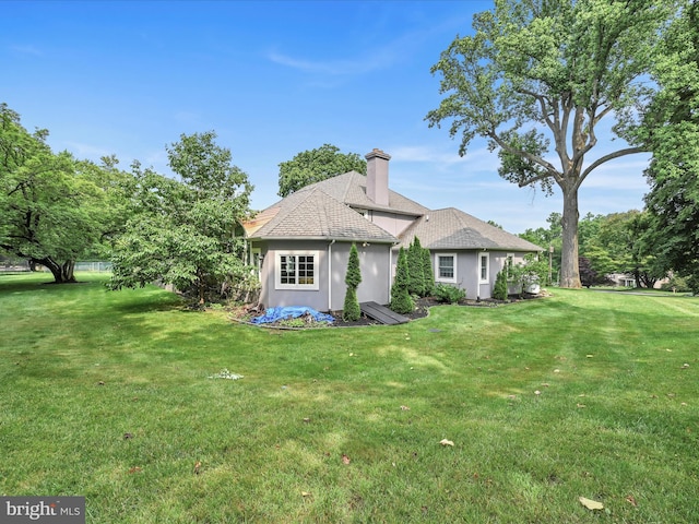 rear view of property with a yard, stucco siding, a chimney, and a shingled roof