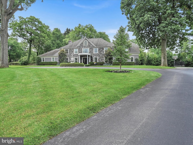 colonial inspired home featuring stone siding, a front yard, and a chimney