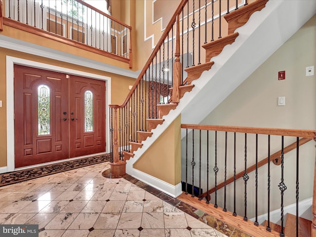 entryway featuring baseboards, inlaid floor details, a towering ceiling, and stairs
