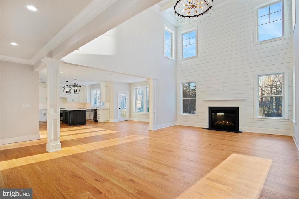 unfurnished living room featuring a chandelier, light wood finished floors, a fireplace with flush hearth, baseboards, and recessed lighting