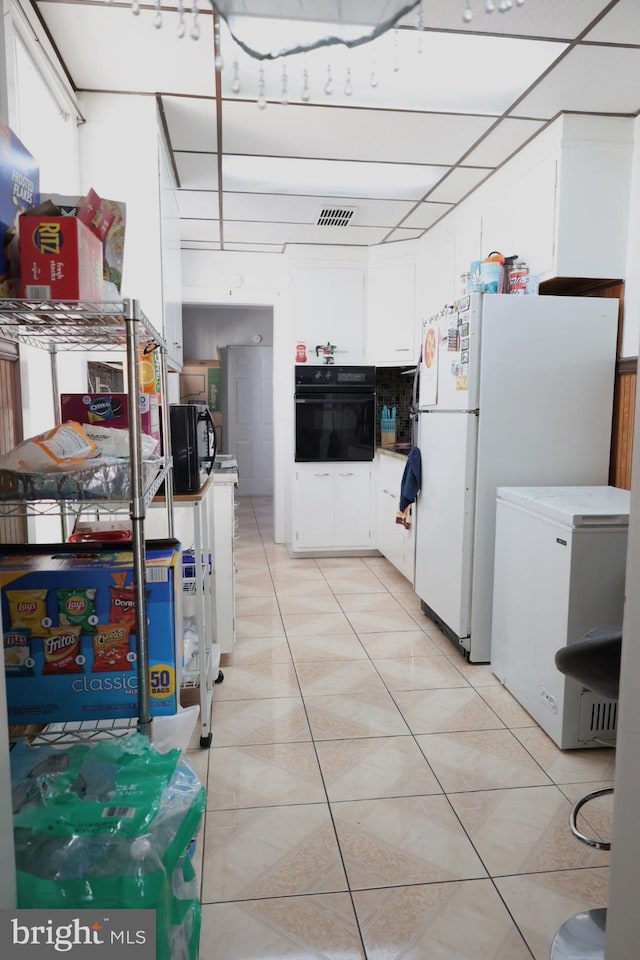 952 Moss St, Reading, PA 19604 - kitchen with black oven, freestanding refrigerator, white cabinets, fridge, and light tile patterned floors