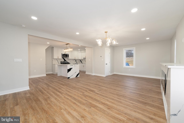 unfurnished living room featuring recessed lighting, a chandelier, baseboards, and light wood finished floors