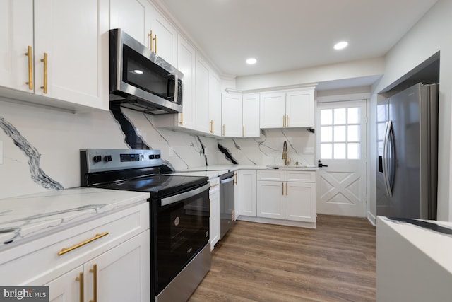 kitchen with appliances with stainless steel finishes, a sink, white cabinets, tasteful backsplash, and wood finished floors