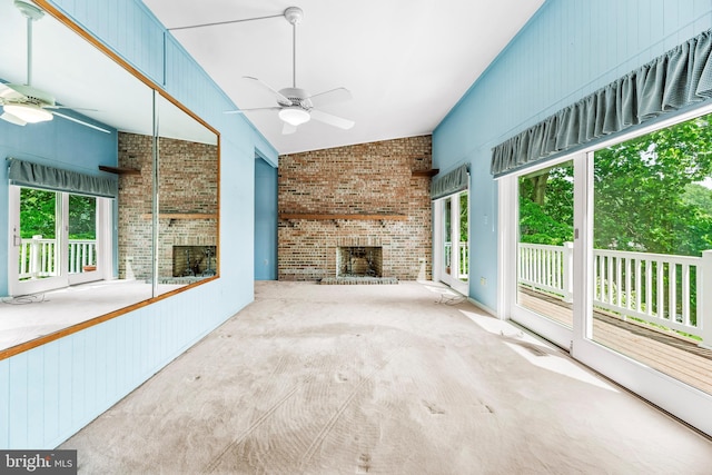 unfurnished living room with a fireplace, a ceiling fan, plenty of natural light, brick wall, and carpet