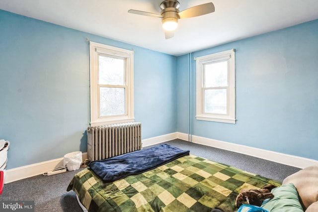 carpeted bedroom with radiator, multiple windows, baseboards, and a ceiling fan