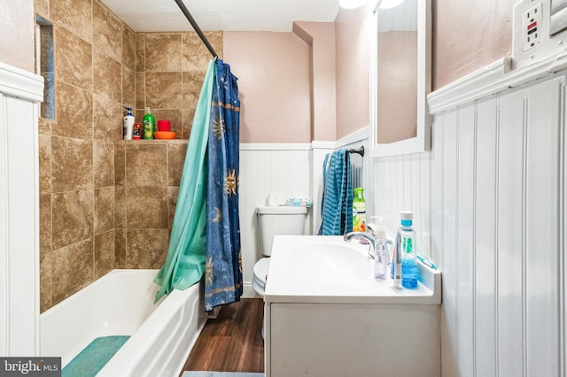 bathroom with wood finished floors, shower / bath combination with curtain, vanity, a wainscoted wall, and toilet