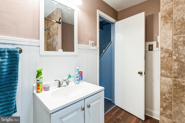 bathroom featuring a wainscoted wall, vanity, wood finished floors, and tiled shower