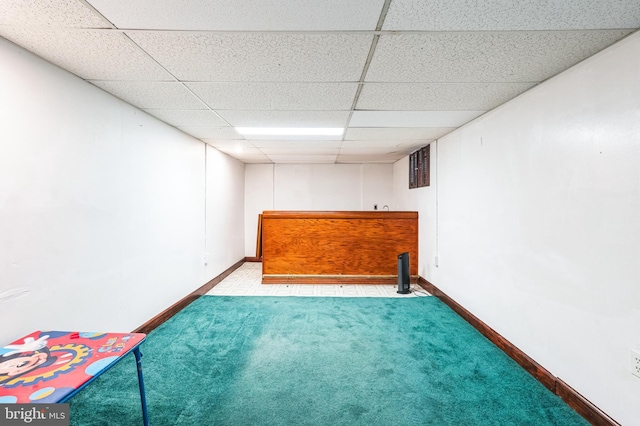 finished basement featuring a paneled ceiling, baseboards, carpet floors, and a dry bar