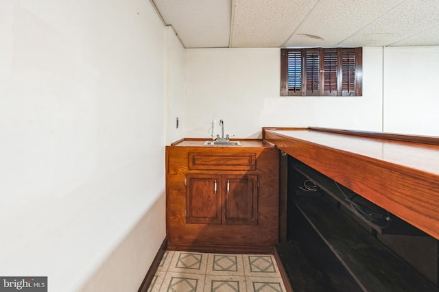 bar featuring a sink, a drop ceiling, and baseboards