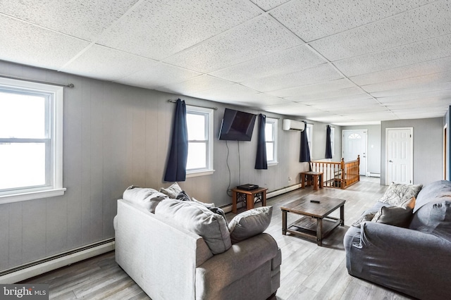 living room with baseboard heating, a wall mounted AC, a drop ceiling, and wood finished floors