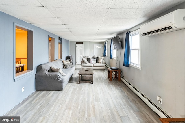 living area with a wall mounted AC, a paneled ceiling, a baseboard radiator, wood finished floors, and baseboards