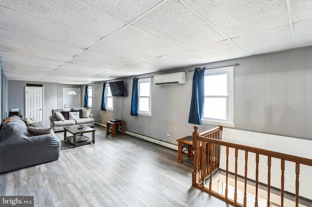 living area with an AC wall unit, a paneled ceiling, wood finished floors, and a baseboard heating unit