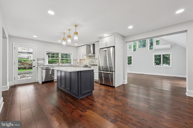 kitchen featuring appliances with stainless steel finishes, wall chimney exhaust hood, light countertops, decorative backsplash, and a kitchen island