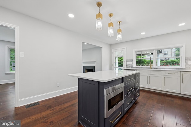 kitchen with white cabinets, light countertops, stainless steel microwave, a fireplace, and hanging light fixtures