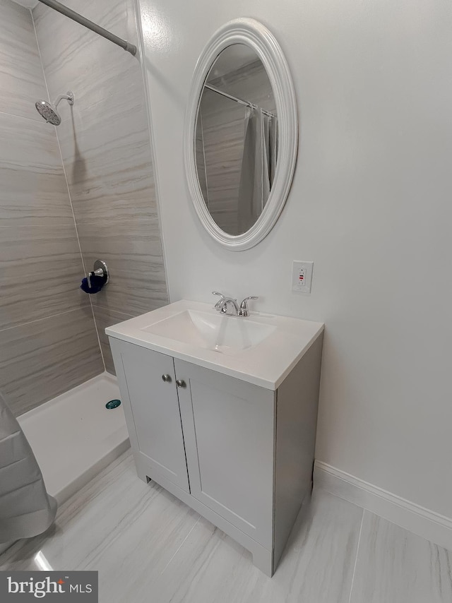bathroom featuring tiled shower, vanity, and baseboards