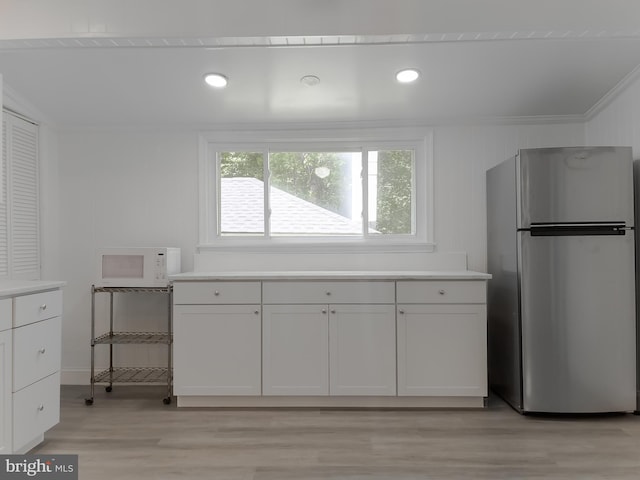 kitchen featuring freestanding refrigerator, white microwave, light wood-style flooring, light countertops, and recessed lighting