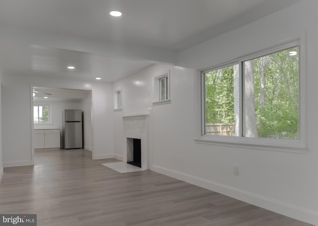 unfurnished living room with baseboards, a brick fireplace, wood finished floors, and recessed lighting