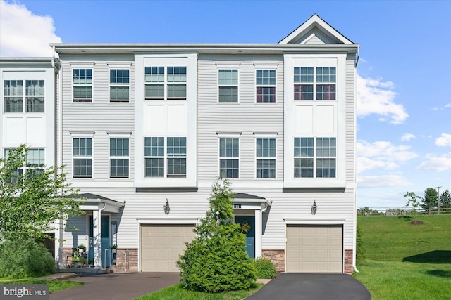 view of property with an attached garage, driveway, stone siding, and a front yard