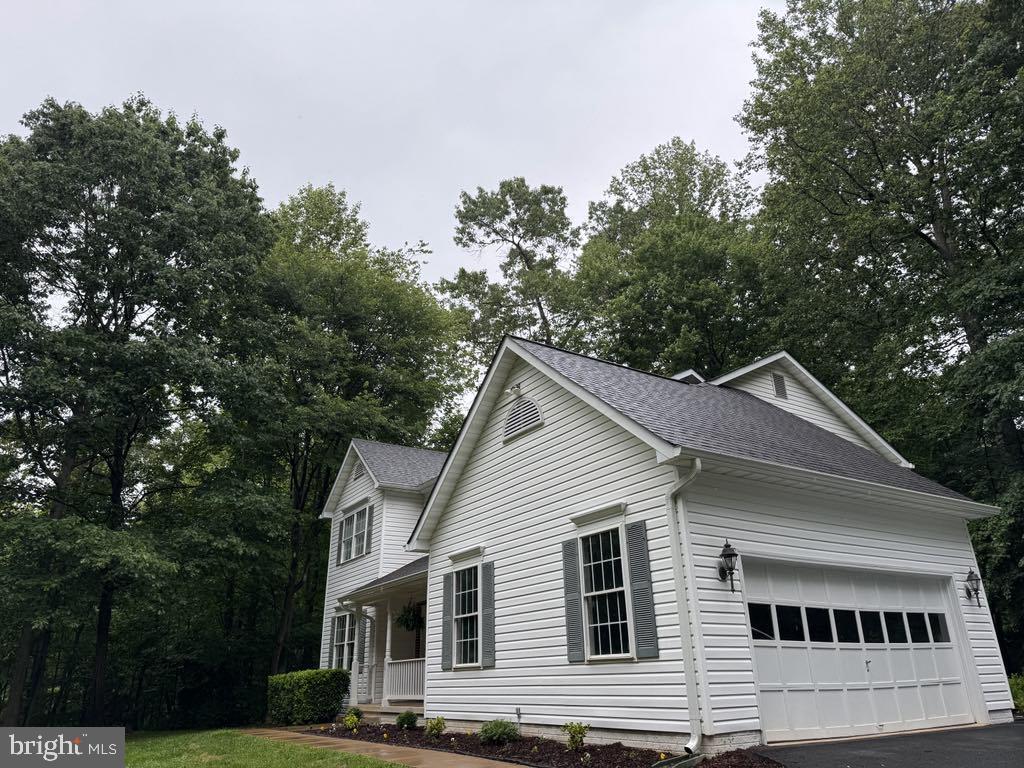 6051 Whippoorwill Dr, Warrenton, VA 20187 - view of property exterior with an attached garage, roof with shingles, asphalt driveway, view of wooded area, and covered porch