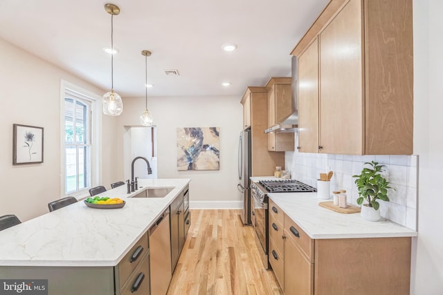 kitchen featuring a sink, stainless steel appliances, light wood-type flooring, an island with sink, and tasteful backsplash